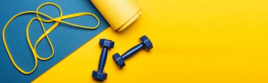 top view of blue fitness mat with dumbbells and resistance band on yellow background, panoramic shot clipart