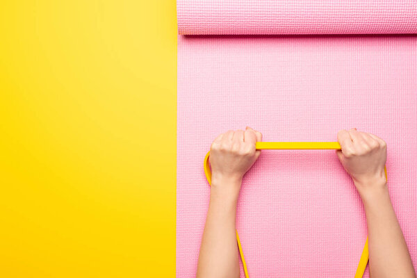 cropped view of woman holding elastic band on pink fitness mat on yellow background