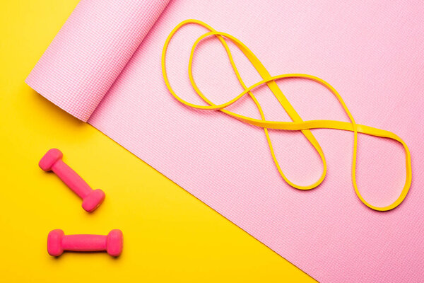 top view of resistance band on pink fitness mat near dumbbells on yellow background