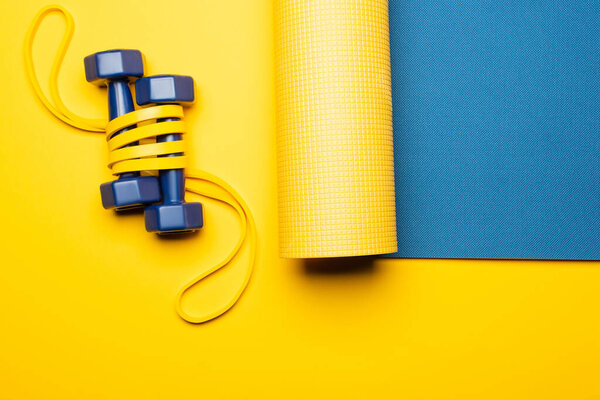 top view of blue fitness mat with dumbbells and resistance band on yellow background
