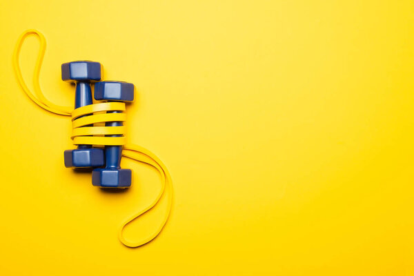 top view of blue dumbbells in resistance band on yellow background