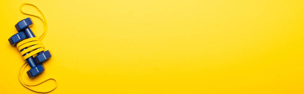 top view of blue dumbbells in resistance band on yellow background, panoramic shot