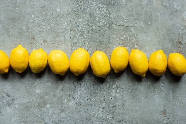 Beton desenli yüzeyde sıralanmış olgun sarı limonların üst görünümü