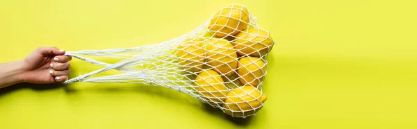 黄色の背景に文字列バッグに熟した全レモンを保持する女性のクロップドビュー — ストック写真