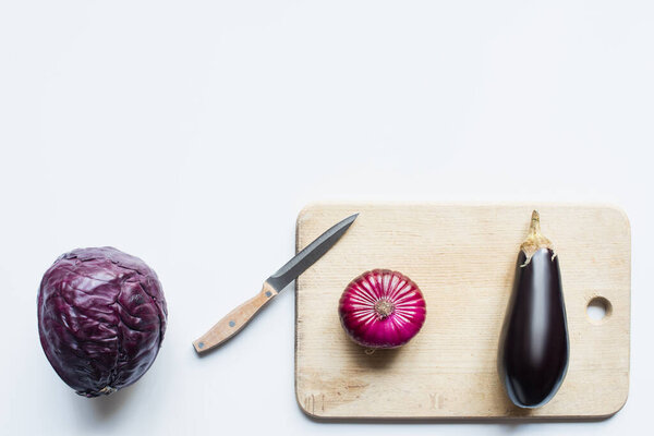 top view of purple whole vegetables, knife and wooden cutting board on white background