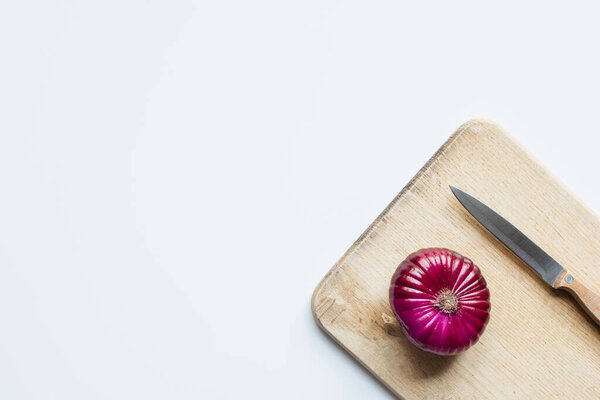 top view of purple whole red onion, knife on wooden cutting board on white background