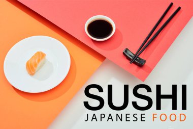 Soya sosu yanında somon somonu, yemek çubuğu ve kırmızı, turuncu, beyaz yüzeye yazılmış suşi Japon yemeği.