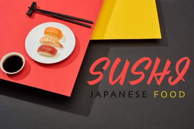 Soya sosu yanında somon, karides ve ton balıklı taze nigiri, yemek çubukları ve kırmızı, sarı ve siyah yüzeye yazılmış suşi Japon yemekleri.