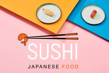 Çubukların yanında ton balıklı ve karidesli taze nigiri ve mavi, pembe, turuncu yüzeye yazılmış suşi Japon yemeği.