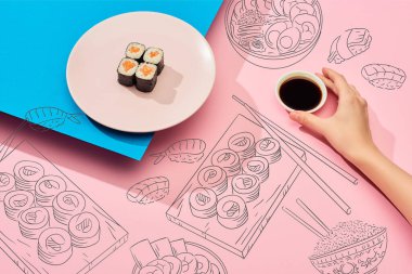 Somon ve suşi resimli taze maki yanında soya sosu tutan mavi, pembe arka planda bir kadın görüntüsü.