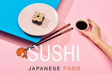 cropped view of woman holding soy sauce near fresh maki with salmon and sushi japanese food lettering on blue, pink background clipart