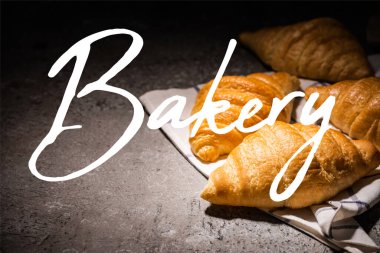 fresh baked croissants on towel near bakery lettering on concrete grey surface  clipart