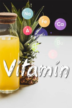 Lezzetli meyvelerin yanında şişede taze ananas suyu ve beyaz ve siyah üzerine vitamin harfleri.