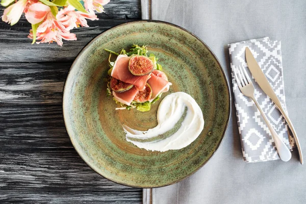 Vista dall'alto del prosciutto gourmet su piatto, fiori e forchetta con coltello su tavolo di legno — Foto stock