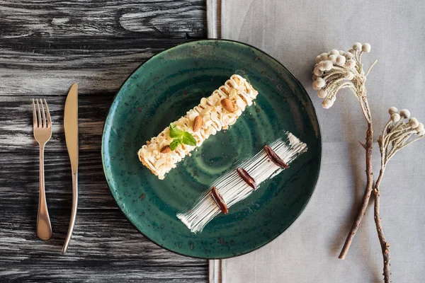 Vista superior da sobremesa doce gourmet com amêndoas e hortelã na placa e garfo com faca na mesa de madeira — Fotografia de Stock