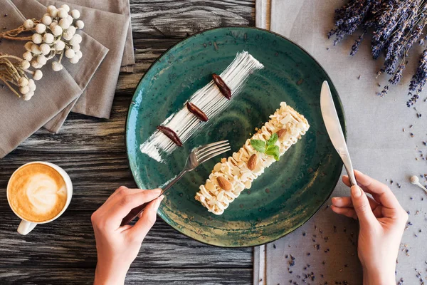 Частичный вид сверху на человека, держащего вилку с ножом и поедающего вкусный сладкий десерт с миндалем — стоковое фото