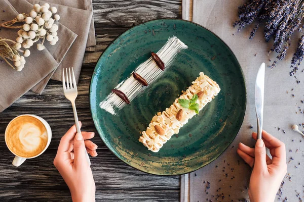 Recortado tiro de persona sosteniendo tenedor con cuchillo y comiendo delicioso postre con almendras - foto de stock