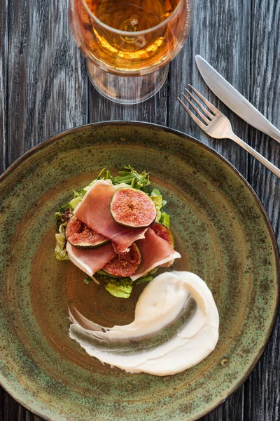 Draufsicht auf köstlichen Prosciutto auf Teller und Gabel mit Messer auf Holztisch — Stockfoto