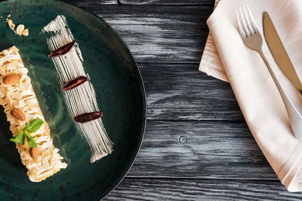 Vista superior de postre dulce gourmet con almendras y menta en plato y tenedor con cuchillo en mesa de madera - foto de stock