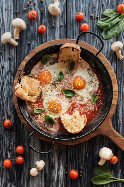 Vista dall'alto di uova arrosto gourmet con formaggio e verdure fresche sul tavolo di legno — Foto stock