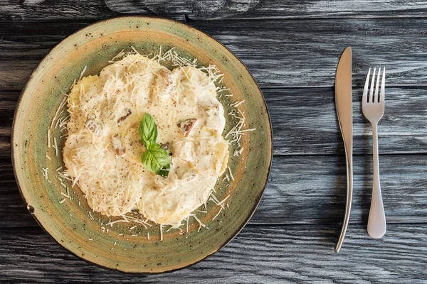 Vista superior de ravioli italiano gourmet com ricota na placa e garfo com faca na mesa de madeira — Fotografia de Stock