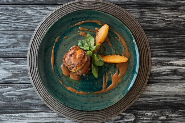 Delicioso bistec de ternera con salsa y hojas de albahaca en el plato en la mesa de madera - foto de stock