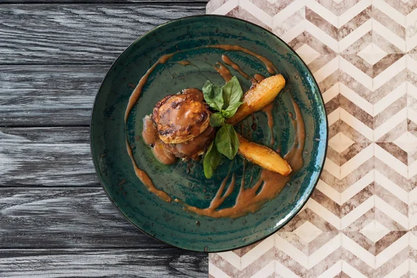 Vista dall'alto di carne deliziosa con salsa e foglie di basilico sul piatto sul tavolo di legno — Foto stock