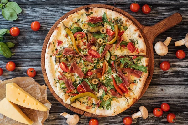 Vista superior de la deliciosa pizza con verduras y carne en tabla de cortar de madera - foto de stock