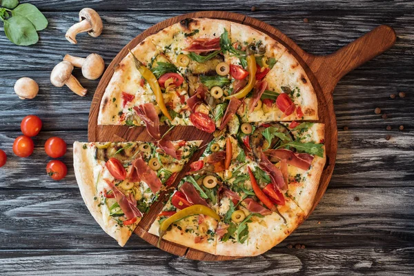 Gourmet sliced pizza with vegetables and meat on wooden cutting board — Stock Photo