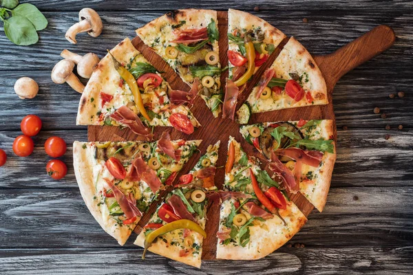 Blick von oben auf geschnittene leckere Pizza mit Gemüse und Fleisch auf einem Holzschneidebrett — Stockfoto