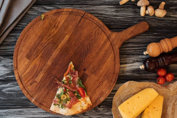 Vista superior de una sola rebanada de pizza sabrosa en la tabla de cortar de madera - foto de stock