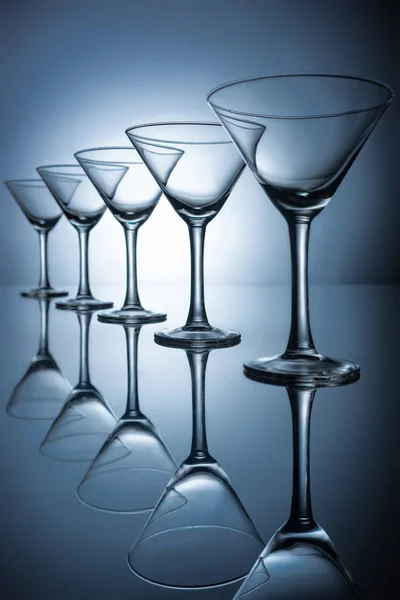 Row of elegant empty martini glasses on grey with reflections — Stock Photo