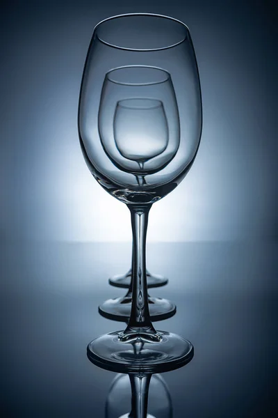 Row of empty wine glasses with reflections, on grey — Stock Photo