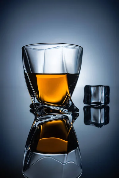 Bicchiere con whisky e cubetto di ghiaccio con riflesso, su fondo grigio scuro — Foto stock