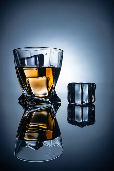 Glass with cognac and ice cubes with reflections, on dark grey background — Stock Photo