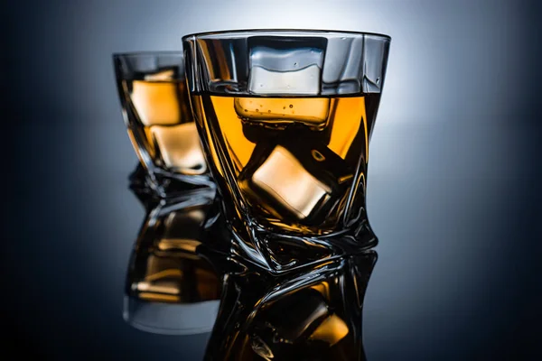 Selective focus of two glasses of cognac with ice cubes, on dark grey background — Stock Photo