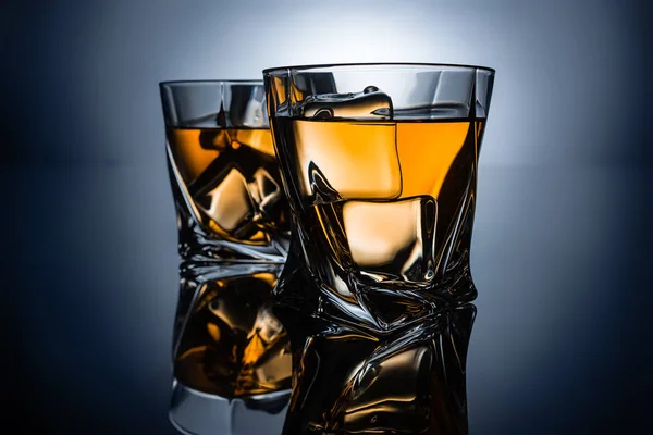 Two glasses of whiskey with ice cubes, on dark grey background — Stock Photo