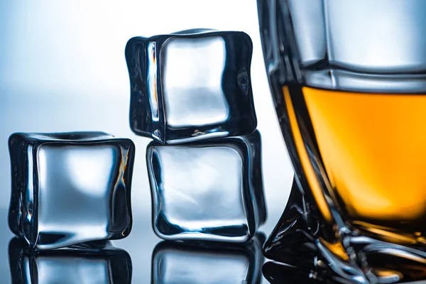 Close up of glass with whiskey and ice cubes near, on grey — Stock Photo