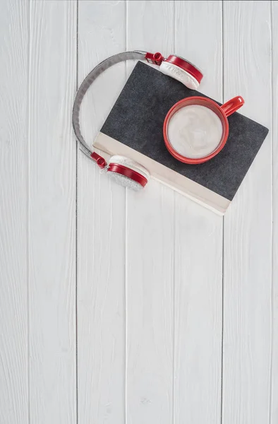 Vista dall'alto di libro, cuffie e coppa rossa su tavolo bianco — Foto stock