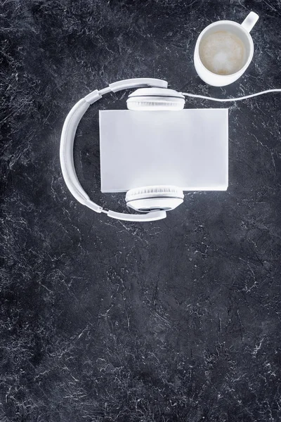 Top view of white book, headphones and cup of coffee with milk on grey tabletop — Stock Photo