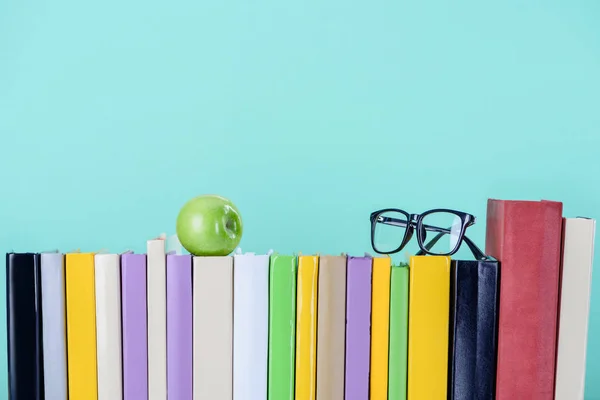 Fila di libri con mela e bicchieri isolati su blu — Foto stock