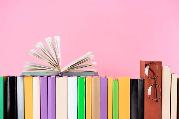 Open book and glasses on row of books isolated on pink — Stock Photo