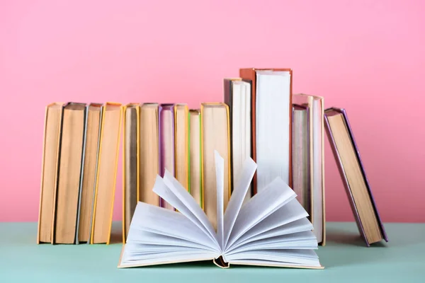 Open book in front of row of books on table on pink — Stock Photo