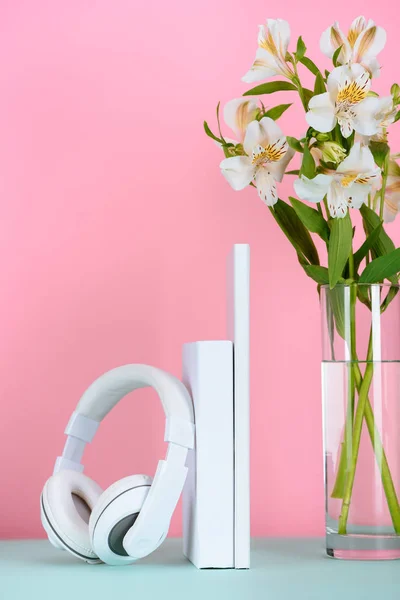Auriculares blancos y libros con ramo de flores en la mesa en rosa - foto de stock