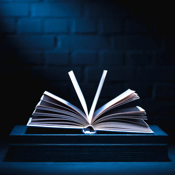 Open book on dark surface with light on pages — Stock Photo
