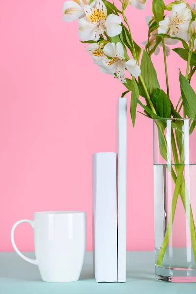 Libros blancos, taza de café y flores en vidrio sobre la mesa en rosa - foto de stock