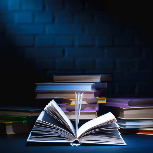 Open book in front of stack of colored books on dark surface — Stock Photo