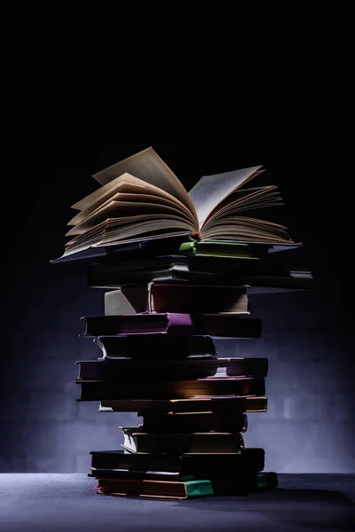 Stack of books with open book on top on dark surface — Stock Photo