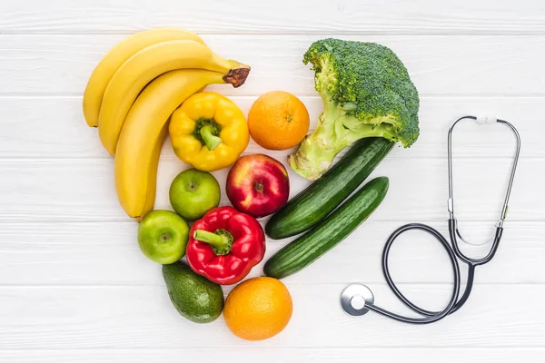 Top view of heart symbol made from fresh fruits and vegetables and stethoscope on wooden surface — Stock Photo