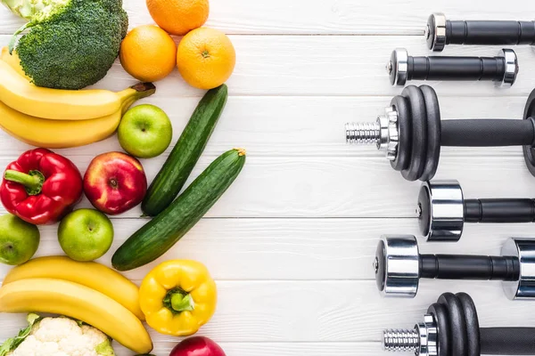 Top view of fresh fruits with vegetables and various dumbbells on wooden surface — Stock Photo
